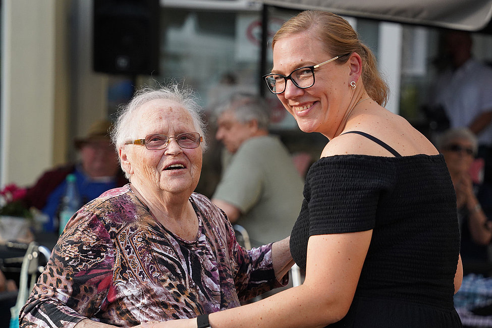 Seniorin und Begleiterin lächelnd beim Sommerfest im Abt-Uhlhorn-Haus